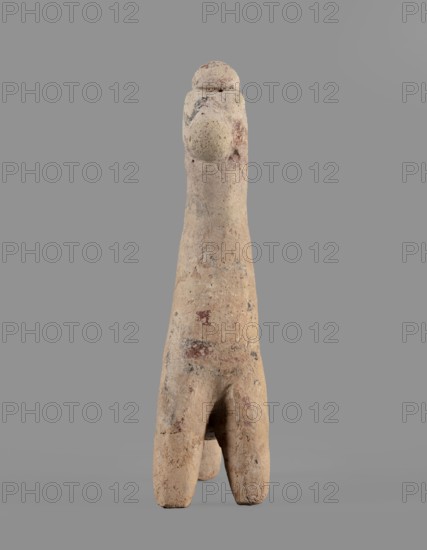 Horse figurine, unknown Cypriot workshop. Schematic horse figurine. Plastically modeled muzzle, strongly rounded at the tip. Eyes marked with convexities. Mane attached. Neck strongly elongated in relation to the rest of the body, flattened at the rear edge, imitating a mane. Body narrow in relation to the neck, cylindrical. Front legs spread out to the sides, also cylindrical. Hind legs designed as a single unit in the form of a cylinder. Traces of polychrome visible on the surface: muzzle and mane reddish-brown, eyes highlighted in black. Traces of black paint also visible on the neck and chest of the animal. 750–600 BC formerly dated 6th century BC; Cypro-Archaic II. Cyprus. Figurine; height 10.8 cm, width 7.8 cm., A roughly vertical beige stone or clay object with a weathered, pitted surface stands against a plain gray background; the object tapers slightly toward the top where a rounded protrusion is visible, and the lower portion splits into a forked base creating a narrow centra...