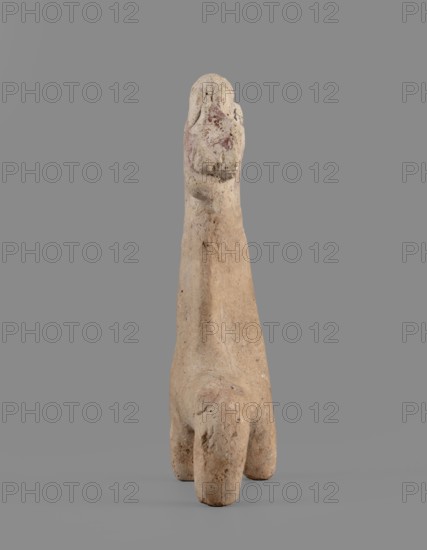 Horse figurine, unknown Cypriot workshop. Schematic horse figurine. Plastically modeled muzzle, strongly rounded at the tip. Eyes marked with convexities. Mane attached. Neck strongly elongated in relation to the rest of the body, flattened at the rear edge, imitating a mane. Body narrow in relation to the neck, cylindrical. Front legs spread out to the sides, also cylindrical. Hind legs designed as a single unit in the form of a cylinder. Traces of polychrome visible on the surface: muzzle and mane reddish-brown, eyes highlighted in black. Traces of black paint also visible on the neck and chest of the animal. 750–600 BC Cypro-Archaic period II, Cyprus. Figurine; height 10.8 cm, width 7.8 cm., A small weathered sculpture with a tall narrow body and a rounded top standing on a base with a few stubby legs, showing a rough textured surface with pitting and erosion; colors visible include beige, tan, light brown, pale gray, and small areas of muted red; the object stands against a smooth ...