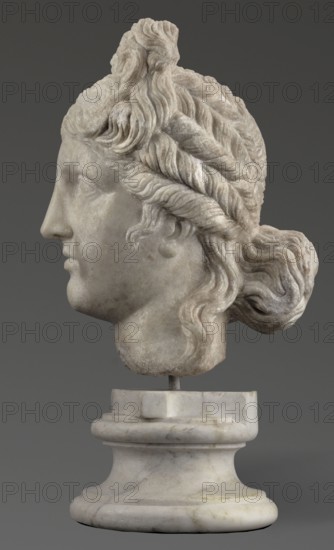 Head of the goddess Aphrodite;, Greek sculpture, female portrait; hair tied in a bow at the front, in a bun at the back; Hellenistic period, 332–30 BC; Greece; sculpture; weight 9.74 kg, A marble sculpted head of a person shown in profile, mounted on a rounded marble pedestal; the sculpture displays detailed wavy and braided hair pulled into a low bun at the back with a short curled lock near the ear, a straight nose, closed lips, and a smooth jawline; the surface shows slight textural weathering and subtle variations in the stone. The visible colors are shades of white and off-white in the marble, with areas of pale gray and faint beige, set against a dark gray background.
