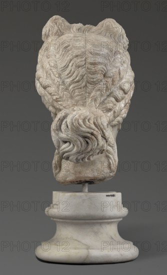 Head of the goddess Aphrodite; maker, Greek sculpture, female portrait; hair tied in a bow at the front and in a bun at the back; 332–30 BC Hellenistic period, Greece; sculpture; weight 9.74 kg, A carved stone bust viewed from the back showing detailed, wavy hair gathered into a twisted bun at the nape, mounted on a rounded stone pedestal; the stone surfaces display shades of off-white, beige, light gray, and subtle brown veining, set against a dark gray background.