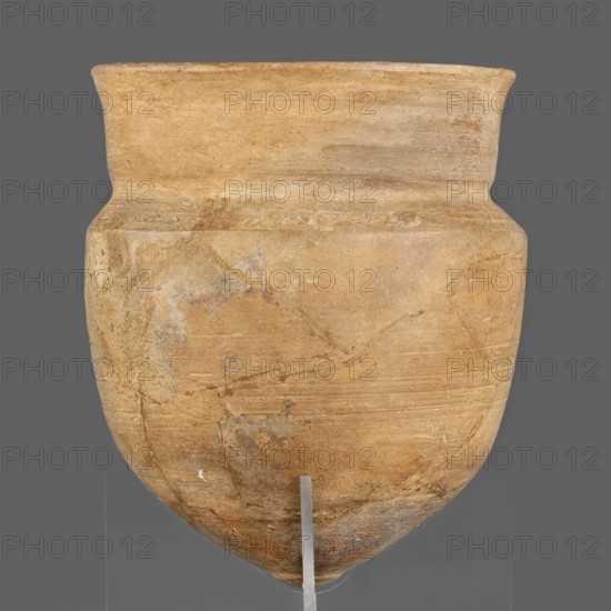 Cup; unknown Neo-Assyrian workshop; palace pottery; Kalah Iraq; cups; Assyrian art; Near Eastern pottery; Eastern Gallic scenography; 9th–7th century BC, Neo-Assyrian period, Northern Mesopotamia Assyria; vessel, A large rounded vessel with a wide flaring rim and a gently tapered body, shown against a neutral gray background; the surface of the vessel is a weathered tan with areas of lighter beige and patches of muted gray, and it displays subtle horizontal tool marks and irregular mineral-like stains; the vessel rests on a clear support with a thin vertical metal rod visible at the bottom center.