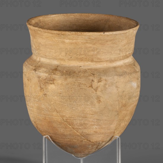 Cup, unknown Neo-Assyrian workshop; palace pottery, Kalah Iraq, cups; Assyrian art, Near Eastern pottery; Eastern Gallic scenography; 9th–7th century BC, Neo-Assyrian period, Northern Mesopotamia Assyria; vessel., A single rounded pottery vessel with a wide flared rim and a narrower shoulder sits on a transparent stand against a solid grey background; the surface of the vessel shows a textured, slightly rough finish with visible scratches and faint repaired cracks, and the colors visible are tan, beige, light brown, and hints of darker brown.