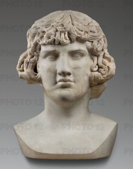 Portrait of Antinous, unknown Roman workshop, male portrait bust, Roman sculpture, 130–138 CE, Roman Empire 27 BC–476, sculpture; weight 59.5 kg, height 54 cm, width 40 cm, depth 32 cm, A carved stone bust of a person shown from the shoulders up with curly, layered hair and a smooth face, the sculpture displaying subtle surface weathering and small discolorations; the hair has carved waves and curls that frame the forehead and ears, and the facial features include closed or carved eyes, a straight nose, and a neutral mouth. The bust rests on a tapered, flat-based plinth. The visible colors are shades of white, off-white, beige, and light tan, set against a neutral gray background.