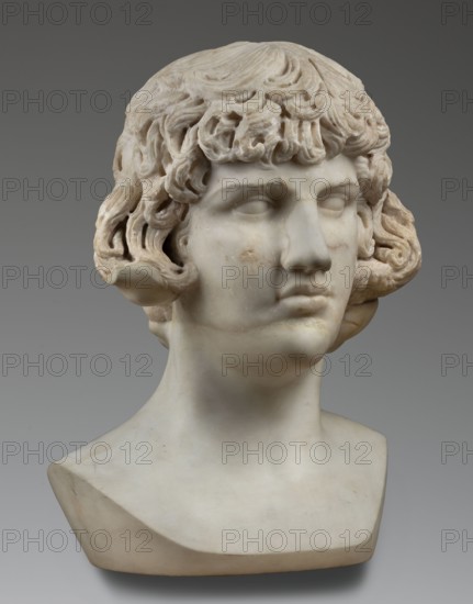 Portrait of Antinous, unknown Roman workshop, male portrait bust, Roman sculpture, 130–138 CE, Roman Empire 27 BC–476, sculpture; weight 59.5 kg, height 54 cm, width 40 cm, depth 32 cm, A marble bust of a young person shown from the shoulders up with curly hair carved in detailed waves and locks, a smooth forehead, closed or blank eyes, a straight nose, and full lips with a slightly downturned expression; the surface shows natural stone texture and a few small areas of discoloration. The sculpture sits on a simple angular base. Visible colors include off-white, cream, light beige, and pale gray against a neutral gray background.