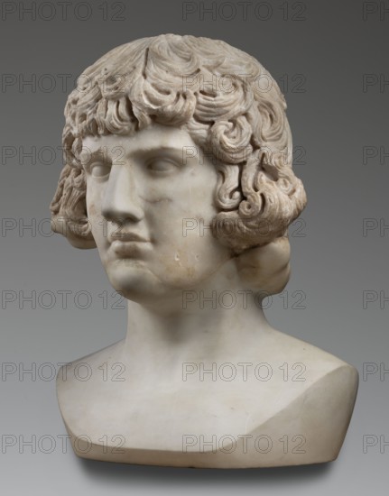 Portrait of Antinous, unknown Roman workshop, male portrait bust, Roman sculpture, 130–138 CE, Roman Empire 27 BC–476, marble sculpture, weight 59.5 kg, height 54 cm, width 40 cm, depth 32 cm, A marble bust of a person shown from the shoulders up with curly, textured hair and a smooth face, rendered in shades of white, off-white, cream, and light beige, set against a neutral gray background; the hair has deeper carved grooves creating shadowed areas that appear slightly darker, and the surface of the bust shows subtle discoloration in warm beige and pale brown tones on the cheeks and neck.