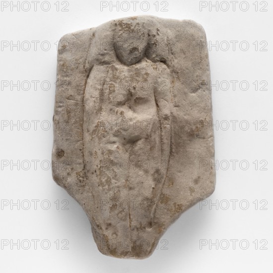 Fragment of a figurine of a woman on a bed. Flat figurine of a concubine resting on a plate imitating a bed; long narrow arms pressed against the body, legs joined. Scen. Gal. Eg.; concubines; figurines of nude women; Egyptian art., Sculpture, ca. 1550–332 BC New Kingdom–Late Period. Tell Atrib; height 8.3 cm, width 5.7 cm., A weathered stone relief in shades of gray and beige shows the raised, simplified outline of a standing humanlike figure with a rounded head and suggestion of shoulders and torso, carved into a roughly rectangular slab with irregular edges; the surface has a rough, pitted texture with patches of darker beige and brown discoloration and worn areas that smooth the carved details, and a few shallow incised lines suggest limbs and folds while the background remains mostly flat and similar in color.