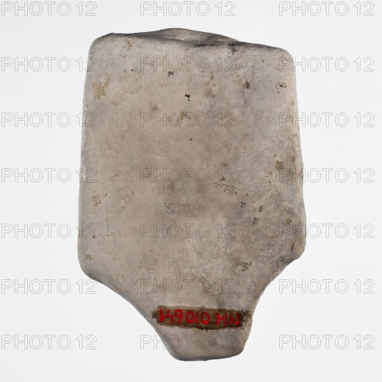 Fragment of a figurine of a woman on a bed. Flat figurine of a concubine resting on a plate imitating a bed; long narrow arms pressed against the body, legs joined. Scen.Gal.Eg., concubines, figurines of nude women, Egyptian art., Sculpture, ca. 1550–332 BC New Kingdom–Late Period. Tell Atrib. Height 8.3 cm; width 5.7 cm., A roughly rectangular stone slab with rounded corners and an uneven bottom edge, showing a smooth but pitted surface with small discolorations and spots; the stone is primarily light gray with areas of beige and brown staining, and there are several darker gray and faint tan patches; the background is white.