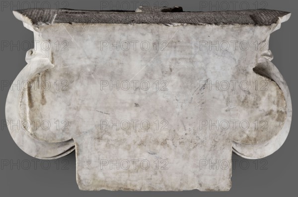 Ionic pilaster capital, unknown Roman workshop, 2nd century, Roman Empire 27 BC–476, architectural element; materials/dimensions: height 27 cm also listed 26 cm, width 46.5 cm, depth 18 cm, weight 19.5 kg., A weathered stone slab with a broad, rectangular top and ornate curved sides sits against a neutral gray background, the stone surface showing a mottled pattern of off-white, gray, and beige with darker smudges and faint scratches; the top edge appears darker and rougher with textured ridges, and the curved side elements flare outward with smoother, slightly shadowed undersides, while the front face displays subtle discoloration, worn patches, and irregular edges along the bottom.