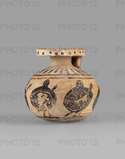 Aryballos with a depiction of warriors with shields, Middle Corinthian period, ca. 570 BC, Corinth; vessel aryballos, height 5.9 cm, width 6.7 cm., An earthenware vessel with a rounded body and a short neck topped by a flat, wide rim; the surface shows painted circular motifs resembling shields or round figures in dark black against a light beige clay background, with additional black linear and dot patterns around the neck and shoulder; the vessel appears worn with areas of surface loss and darkened spots, and the visible colors are beige, black, and hints of brown.