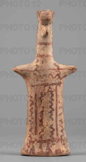 Female idol, Female idol with arms marked as appendages. On a long cylindrical neck is a nose and an upward-curved strand of hair with a diadem. The robe, breasts, and hair are rendered with a varnish line. 6th century BC previously dated 7th century BC. Boeotia. Terracotta figurine. Height 16.7 cm; width 7.6 cm; depth 3 cm; weight 0.15 kg., The image shows a standing figurine-shaped object with an elongated neck and a small head, flared horizontal arms near the top, and a tapered body that widens slightly at the base; the surface appears worn and textured with irregular paint patterns in shades of brown and reddish-brown on a tan or beige clay background, with wavy and linear decorative motifs running vertically and horizontally across the body; the head and neck have faint reddish markings and the overall object casts a soft shadow on a neutral gray backdrop.