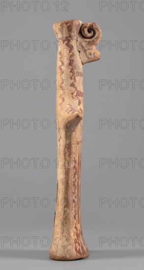 Female idol, Female idol with arms marked as appendages. On a long cylindrical neck is a nose and an upward-curved strand of hair with a diadem. The robe, breasts, and hair are rendered with a varnish line. 6th century BC formerly dated 7th century BC. Boeotia. Terracotta figurine; height 16.7 cm, width 7.6 cm, depth 3 cm, weight 0.15 kg., A tall slender carved object standing upright against a plain background, with a flared base and a slightly rounded top that transitions into a curled spiral element on one side; the surface shows irregular, wavy painted motifs running along its length and areas of worn, uneven texture. The visible colors include beige, light tan, reddish-brown, and muted gray, with patches where the original surface appears faded or chipped. The form has a protruding small ledge-like feature about midway up and subtle vertical ridges and indentations along its shaft, with the spiral detail showing concentric curves and a rough, weathered finish.