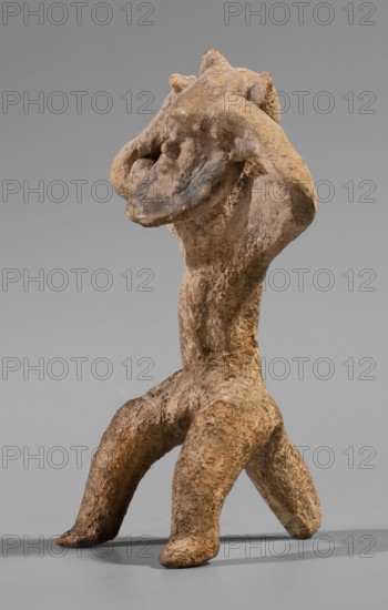 Satyr figurine. Clay figurine depicting a satyr with a face stylized as a mask with protruding ears and two horns. The man is shown in an unnatural pose — crouching with legs widely apart, supported by a thick tail. The hands are raised upwards, emphasizing and exposing the figure's genitals. The satyr's hands touch the figure's head, which is tilted slightly to the left. The face is characterized by lush, regular facial hair. The figure's eyes are small. The eyebrows and broad nose are clearly defined. The figure's thin mouth is closed. Both the hands and legs are treated schematically in comparison to the carefully modeled face. The fine-grained clay from which the figurine was made has a yellowish tint. 5th century BC previous datings: 2nd half of the 6th century BC–beginning of the 5th century BC; earlier: end of the 6th century BC–first half of the 5th century BC. Origin: Corinth. Dimensions: height 8.8 cm, width 4.8 cm, depth 4.4 cm; weight 0.04 kg. Creator: unknown., A roughly t...