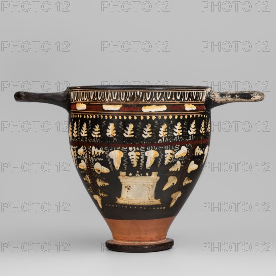 Gnathian skyphos with depiction of an altar, Gnathia style, Southern Italic pottery, ca. 340–320 BC, Southern Italy, skyphos vessel, weight 0.168 kg, iconography: altar., A black ceramic vessel with a rounded body tapering to a narrow foot and a short pedestal, featuring a pair of horizontal handles extending from opposite sides; the lower foot and a band near the base show reddish-brown clay, while the main body is coated in black and decorated with pale yellow and cream painted motifs including stylized leaf shapes and abstract forms arranged in horizontal bands; a narrow red band encircles the upper portion beneath the rim, and the rim area displays a pattern in cream and black; the handles and rim show areas of wear with lighter patches.