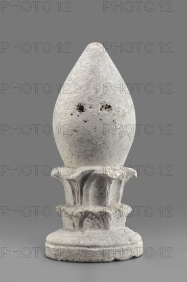 Pine cone-shaped cippus;, classified Gallo-Classical scenography; architectural, sepulchral funerary architecture; acanthus ornament; Etruria Italy; cippus with echinus-shaped base from which a double acanthus wreath topped with an egg-shaped element grows; 4th–3rd century BC; Praeneste Italy; varia; height 32.3 cm; width 15.2 cm; weight 6.9 kg, A sculpted stone object resembling an elongated teardrop or bud set on a decorative base, with a rough, pitted surface texture and visible small holes; the piece appears in shades of off-white and light gray with some darker gray speckles, and it sits against a flat medium-gray background.