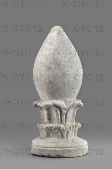 Pine cone-shaped cippus;, classified as Gallo-Classical scenography, architectural elements, sepulchral funerary architecture; acanthus ornament; Etruria Italy; cippus with echinus-shaped base from which a double acanthus wreath topped with an egg-shaped element grows; 4th–3rd century BC; Praeneste Italy; height 32.3 cm, width 15.2 cm, weight 6.9 kg., A carved stone object with a rounded, pointed top sitting on a flared, decorative base; the stone surface appears rough and weathered with visible irregular texture and small pits, and the base has carved, petal-like motifs and layered circular platforms. The visible colors are shades of gray, off-white, and subtle beige.