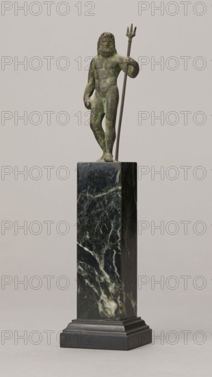 Figurine of Poseidon, unknown Roman workshop. Figurine of Poseidon standing in contrapposto, resting on a trident. The weight of the body rests on the left leg; the right is slightly moved back, the foot bent at the toes. The body is nude, correctly modeled, with clearly defined abdominal muscles. In the left hand the figure holds a trident; the right hand is lowered at the side of the body, holding a cylindrical object at hip level. The head is slightly bowed. The face is framed by long hair and a beard. 1st century, Roman Empire 27 BC–476. Bronze figurine; height 8.7 cm, width 3.5 cm, depth 1.8 cm, weight 0.362 kg with base., A small greenish bronze statuette of a bearded nude male figure stands on a tall rectangular dark green and black marble pedestal; the figure holds a long thin staff ending in a three-pronged spear and has a weathered patina with areas of darker and lighter green, while the pedestal shows veining in white and lighter green and rests on a stepped black base again...