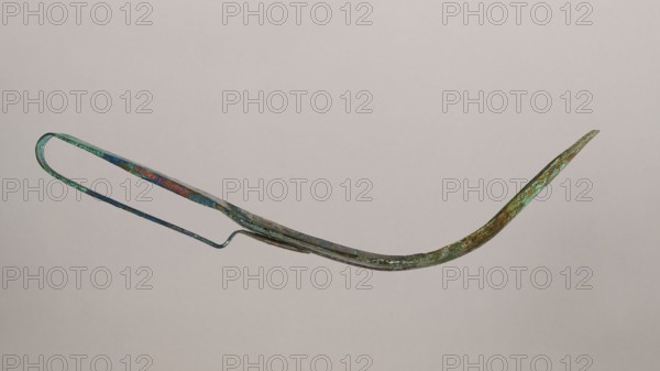 Scraper, metal scraper with a typical, slightly curved shape consisting of a handle and a blade with a slightly rounded end. 6th–4th century BC, possibly Rome; tool. Height 4.5 cm, width 28 cm, depth 11 cm, weight 0.11 kg., A slender curved metal object with a looped handle at one end and a tapered pointed tip at the other, showing surface irregularities and corrosion. The metal displays colors including green, turquoise, blue, brown, and hints of rusty orange, with mottled patches and areas of patina. The object has a narrow elongated body with a slight S-shaped bend near the handle and a thin supporting arm running along its length. The background is a plain light gray-beige.