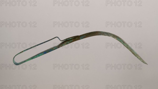 Scraper, Metal scraper with a typical, slightly curved shape consisting of a handle and a blade with a slightly rounded end. 6th–4th century BC, possibly Rome; tool. Height 4.5 cm, width 28 cm, depth 11 cm, weight 0.11 kg., An elongated curved metal object with a narrow looped end and a pointed tip, showing a weathered surface with patches of green and blue patina alongside areas of brown and dark metal, photographed against a light neutral background.