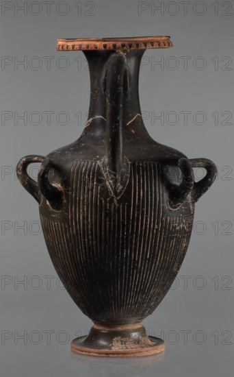 Black-finned hydria with fluting, unknown Apulian workshop. Hydria with fluting belly. Red clay. Black and shiny engobe firnis. The rim widens and turns outward, decorated with a painted ornament called an ovoid oxeye. The neck is long, cylindrical, decorated with a gilded garland painted at the base. The shoulders are clearly defined. The belly is oval, tapering towards the base, covered with fluting, impressed from the mold. The handles are cylindrical, attached vertically at shoulder height. Wide base. Preservation condition: cracked engobe in places, gilding worn away. 320–310 BC, Apulia, hydria, vessel, height 57 cm, width 24.7 cm, A tall ceramic vessel with a narrow neck and flared rim sits against a neutral gray background; the vessel is predominantly black with terracotta-colored edges and worn areas, showing a few lighter scratches and chips. The body has a ribbed texture created by several vertical grooves running from the shoulder to the lower belly, and there are a few roun...