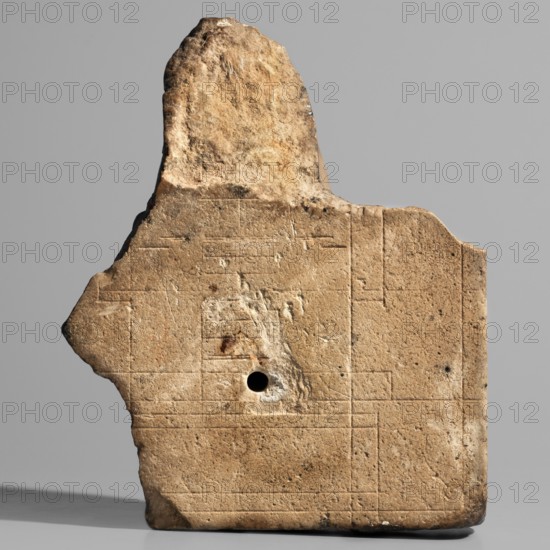 Sculptural model — head of Nectanebo I or II. Sculpture model of a ruler's head in full relief attached to a flat slab background fragmentarily preserved on the right. The ruler wears a nemes covering half the forehead, decorated at the front with a uraeus whose body is curled in a horizontal zigzag similar to a figure-eight with a straight tail. The nemes bears twisted ram's horns. The face is oval and plump with rounded chin and cheeks; small mouth with upper and lower lips of equal width and slightly upturned corners; long nose; small, close-set, slightly slanting eyes with upper and lower eyelids highlighted by thin lines; wide eyebrows. Very careful modeling with precisely executed details; auxiliary lines visible on the back. With base. Height 13 height 11 cm, width 9 cm, depth 5 cm, weight 0.338 kg. 380–343 BC; Late Period, 30th Dynasty reign of Nectanebo I or II; Egyptian sculpture., A weathered stone fragment with an irregular top edge and a roughly triangular protrusion on on...