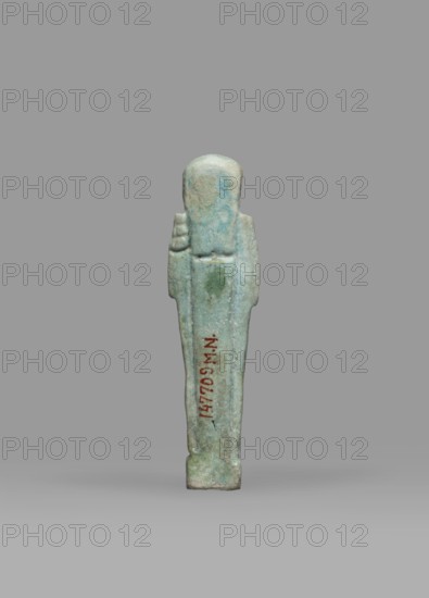 Ushabti, Mummy-shaped funerary figurine shabti, standing on a base, back supported by a pillar/pilaster. Arms crossed on the chest, the right folded over the left; both hands holding hoes. A bag is on the back, slung over the left shoulder on a single string. Wears a three-part smooth wig back strand longer than front strands. Long, straight, wide beard. Large eyes, wide nose, mouth set in a grimace, very large ears. No inscription. Late Period, Egypt, 664–332 BC. Height 7.7 cm, width 2.1 cm., A small upright figurine with a smooth rounded head and simplified body stands against a plain gray background; the figure is predominantly light blue-green with areas of pale turquoise and subtle greenish patches, and there is a narrow darker reddish-brown vertical detail on its front; the surface appears worn and slightly pitted, and the base is a muted gray-green.