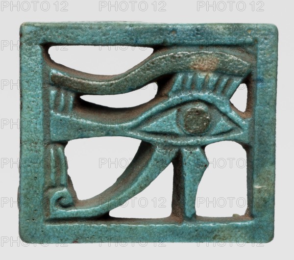 Amulet — Eye of Horus. Openwork Eye of Horus in a rectangular frame; iris and eyebrow black, the rest green-blue. Amulet, ca. 945–656 BC Third Intermediate Period, 22nd–25th Dynasty. Height 2.9 cm; width 3.4 cm. Found at Edfu., A small rectangular object with an openwork design showing a stylized eye motif, rendered within a bordered frame; the surface has a textured, slightly pitted appearance and shows wear at some edges. The object is primarily turquoise with areas of darker teal and small spots of brownish discoloration. The carved lines form curved and angular shapes, including an almond-shaped eye, a circular raised area at the eye center, and decorative strokes above and below the eye. The interior cutouts create negative space against a light neutral background.