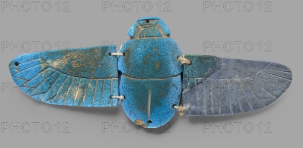 Winged scarab; flat-bottom scarab with attached wings right wing possibly completed or chipped glaze; mummiform motif; scarab amulet; Late Period, Egypt, 664–332 BC; height 6 cm, width 15.5 cm, depth 1 cm., An object resembling a spread-winged scarab composed of a central rounded body and two elongated wing-like pieces, all connected with short pieces of twine; the surface shows a mottled mix of bright turquoise blue and darker teal with areas of worn, sandy beige and gray; the left wing is predominantly bright blue with incised feather-like lines and patches of sandy beige wear, the right wing transitions from teal into a muted gray-blue with similar incised lines and slight surface encrustation, and the central body block is a richer turquoise with darker speckling and small worn beige spots, while the twine is a natural beige color.