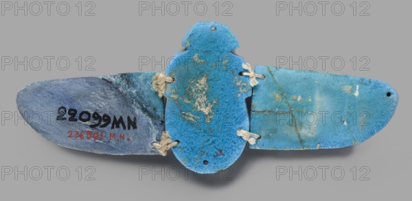 Winged scarab, flat-bottom scarab with attached wings right wing possibly completed or with chipped glaze; scarab amulet, glazed faience; Late Period, Egypt, 664–332 BC; height 6 cm, width 15.5 cm, depth 1 cm; motifs: wings, mummiform scene., A flat, wing-shaped object composed of three connected blue ceramic pieces with a central rounded form and two elongated side panels, joined by pieces of coarse beige twine threaded through holes; the surfaces show mottled shades of blue ranging from light turquoise to deeper cyan with areas of pale greenish blue and small patches of beige and brown discoloration; the left panel appears more muted bluish-gray with a rough texture and the central piece has speckled darker blue spots and irregular beige deposits, while the right panel shows a smoother, lighter turquoise surface with fine hairline cracks and some brownish stains; the background is a uniform light gray.