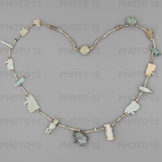 Necklace with amulets, udjat eyes, tit knots, Ptah the dwarf mythology, Toeris mythology, necklaces, columns, auletes separated by tubular and disc-shaped beads: 8 udjat eyes, Isis knot, Toeris, papyrus column, Ptah the dwarf, 2 anthropomorphic deities, 2 plaques, ca. 1550–332 BC; New Kingdom–Late Period, Egypt, amulet, height 70 cm, A heart-shaped arrangement of a necklace composed of a string of small cylindrical and disc beads in muted beige and light tan tones, interspersed with a few pale green and turquoise beads, and adorned with several flat, shaped pendants in varying shapes and sizes; the pendants show colors including pale blue-green, light turquoise, bluish-gray, cream, and a darker weathered turquoise with brownish patina, and exhibit irregular worn surfaces and carved or cut outlines; the background is a uniform medium gray.
