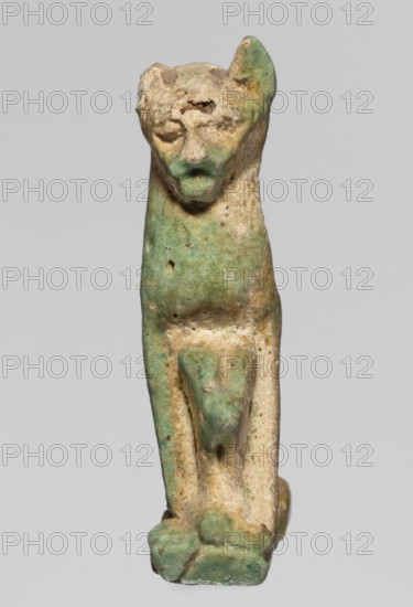 Amulet — cat; maker, cats; pendant; amulet; material unspecified; ca. 945–525 BC 22nd–26th Dynasty, Egypt; height 3.3 cm, width 2 cm., A small weathered figurine of an animal-like form with a rounded head, pointed ears, and a simplified face, standing upright on a narrow rectangular base; the surface shows a mottled mix of green and beige tones with areas of darker and lighter green patina, pitted and rough textures, and some smoother worn spots, with the limbs and body rendered in a stylized, blocky manner and the overall appearance suggesting age and abrasion.