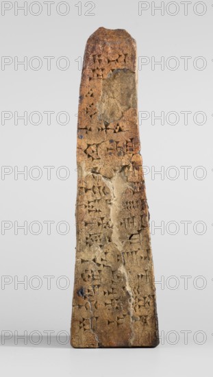Votive obelisk with an inscription of King Ashurbanipal forgery with a copy of an ancient text, cuneiform writing, Ashurbanipal king of Assyria; ca. 668–ca. 631 BC, votive offering obelisk, inscriptions, forgery. Clay votive obelisk tapering toward the top; cuneiform text inscribed on all four faces. Dating of copied inscriptions: c. 668–c. 631 BC Neo-Assyrian period; forgery dated 2nd half 19th century–1st half 20th century. Based on inscriptions from Iraq Quyunjik, Nineveh. Probable place of creation unknown forgery; likely Middle East. Function: dedication/document. Height 13.1 cm; width 3.7 cm; thickness 4.2 cm., A tall, narrow stone object with a tapered, slightly rounded top stands upright against a pale gray background, its surface showing a weathered, uneven texture with visible cracks and chips. The stone displays a range of earthy colors including tan, light brown, rusty brown, and small patches of darker brown, with a few lighter beige areas where the surface appears more wo...