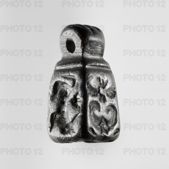 Stamp seal with figural representations. Glyptic, stamp seal in the form of a truncated pyramid on a square base, terminated with a round handle. The four side walls and the base are engraved with stylized figurative representations: two opposite sides show a rider on a horse; one of the other sides depicts a striding figure holding a staff topped with a star; the opposite wall depicts an animal being attacked by a bird of prey. A winged animal is engraved on the seal's base. Iron Age, 9th–6th century BC; Northwestern Syria, Near East. Seal impression carrier dimensions: length 8.5 cm, width 4.4 cm. Seal dimensions: height 2.8 cm, width 1.3 cm, depth 1.4 cm., A small dark gray and black carved object with a rounded top that has a hole through it, a vertical ridge down the center, and a textured lower portion showing carved floral and curved decorative motifs on either side, set against a light gray background.