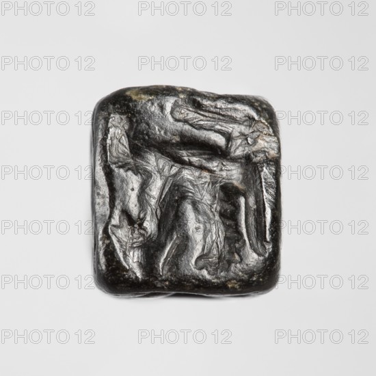 Stamp seal with figural representations. Glyptic stamp seal in the form of a truncated pyramid on a square base, terminated with a round handle. The four side walls and the base are decorated with engraved, stylized figurative representations: two opposite sides depict a rider on a horse; one side depicts a striding figure holding a staff topped with a star; the opposite wall depicts an animal being attacked by a bird of prey. A winged animal is engraved on the seal's base. Iron Age, 9th–6th century BC; Northwestern Syria, Near East. Seal; height 2.8 cm, width 1.3 cm, depth 1.4 cm; impression carrier dimensions: length 8.5 cm, width 4.4 cm., A small square object with rounded corners sits centered on a light gray background; the object has a dark metallic sheen with visible highlights in silver and subtle areas of dull greenish and brownish tones, and its surface shows irregular raised and recessed textures forming abstract, crumpled patterns.
