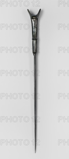 Dagger, unknown Luristan workshop. Dagger with a cast blade and a mushroom-shaped hilt with a rimmed mount; the raised edges of the mount served to hold a lost hilt casing, which may have been made of bone, wood, horn, or stone. The hilt shaft is richly profiled and flows directly into the blade with a centric point. Behind the short, rectangular base, blunted on both sides, the double-edged blade tapers evenly toward the tip. A slightly convex ridge runs through the center of the blade and splits along one-third of its length toward the base, creating a triangular flat field. 9th–6th century BC; Iron Period II 1st half of the 1st millennium BC. Luristan, Iran. Weapon. Height 33.8 cm; width 2.9 cm; depth 0.8 cm; weight 194 g., A long slender metal object with a dark, metallic finish that shows areas of black, dark gray, and hints of green; the top end has a forked, Y-shaped section attached to a thicker handle-like portion that tapers into a rounded connector before transitioning into ...