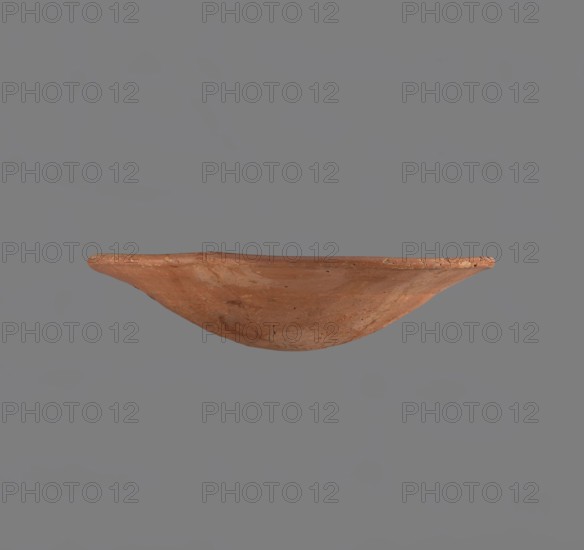 Bowl, Low bowl with irregular, strongly flaring walls and a rounded bottom. Rounded rim, slightly rolled outward. Surface smoothed and covered with a layer of red engobe. Bottom worked with a tool. Hand-made. Vessel glued together from several fragments. Comparative typology: types XXVII–XXVIII Old Kingdom, c. 2686–2181 BC, similar vessels from Edfu; dimensions: height 6.1 cm, rim diameter 28.3 cm, body diameter 28.3 cm., A shallow, rounded bowl-like object with a worn, uneven rim shown in profile, displaying a textured surface with patches of lighter and darker areas; the object is primarily terracotta orange with spots of brown and pale beige, set against a uniform gray background.