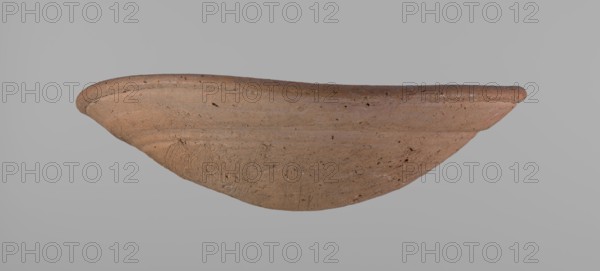 Shallow bowl of rounded, asymmetrical shape with a rounded, flaring, irregular rim. Surface is level; lower part finished to approximately half its height with a knife or similar tool. Slightly above the middle, a horizontal line likely from placement on a stand. Dark red clay; complete. From Edfu, local workshop. Old Kingdom, ca. 2686–2181 BC. Dimensions: height 7.2 cm, rim diameter 26.2 cm., A shallow, curved clay vessel displayed against a plain gray background, showing a rough, textured surface with visible tool marks and small pits; the vessel is primarily terracotta brown with variations including lighter beige and slightly darker brown areas, and there are hints of reddish and grayish tones in some spots.