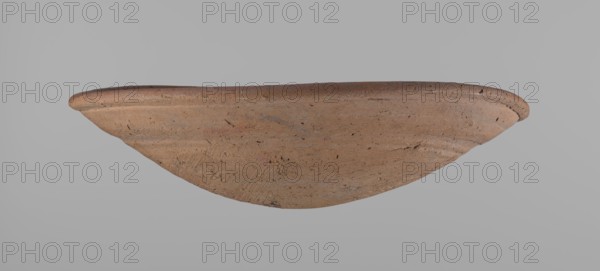 Bowl, Shallow, rounded, asymmetrical clay bowl with a flaring, irregular rim. Surface is level; lower half of the interior finished with a knife or similar tool. Slight horizontal line slightly above mid-height, likely from placement on a stand. Dark red color. Vessel complete. From Edfu, local workshop. Old Kingdom, ca. 2686–2181 BC. Dimensions: height 7.2 cm, rim diameter 26.2 cm. Comparative reference: A. Reisner, fig. 227 35-8-16., A wide, shallow clay bowl viewed from the side, showing a rounded rim and a curved body with a slightly rough, pitted surface; the clay appears in shades of brown and tan with small darker flecks, and the background is a flat light gray.