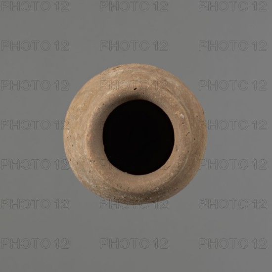 Vessel with hieratic inscription, Egyptian pottery. Conical clay vessel tapering towards the bottom, irregular, widest approx. 3/4 of the height. Narrow, sloping shoulders; short, wide neck; very gently rounded, slightly flaring rim; pointed bottom. Handmade, upper part neck and rim turned. Surface even, outer probably covered with a layer of engobe. Made of Nile clay NB2 Vienna System. In the central part of the belly there are remains of a hieratic inscription in black probably sht dwdw. The vessel is complete and well preserved; traces of salting on one side of the belly. Old Kingdom, Edfu. Height 16.1 cm, rim diameter 6.3 cm, body diameter 8.4 cm. Comparative parallels cited; earlier dated to the 4th–5th Dynasty; ca. 2686–2181 BC., A round, top-down view of a weathered clay vessel with a wide, dark opening at its center; the vessel shows a textured, rough surface in shades of brown and tan with small pits and variations, set against a flat gray background.
