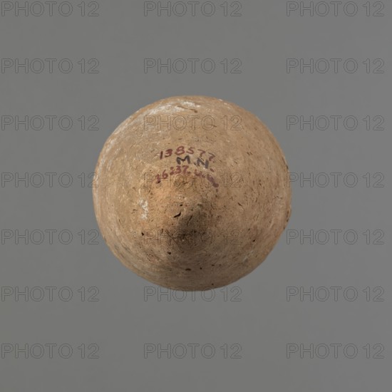 Vessel with hieratic inscription, Egyptian pottery. Conical clay vessel tapering toward the pointed bottom; irregular, widest at approx. 3/4 of the height. Narrow, sloping shoulders; short, wide neck; very gently rounded, slightly flaring rim. Handmade with the upper part neck and rim turned. Surface even, outer layer probably covered with engobe. Made of Nile clay NB2 Vienna System. In the central part of the belly are remains of a hieratic inscription in black probably sht dwdw. The vessel is complete and well preserved, with traces of salting on one side of the belly. Old Kingdom, ca. 2686–2181 BCE. Dimensions: height 16.1 cm; rim diameter 6.3 cm; body diameter 8.4 cm. Comparable examples: Petrie, Dendera; Hope, Akhmim type AIVa 2bi; Reisner; Brunton type 77N; Mace, Naga ed-Der; Petrie, Abydos II; Keiser, Avila, Dreyer, Jaritz, Laskowska-Kusztal, MDAIK 40., A rounded, slightly pointed object with a rough, weathered surface in shades of brown and tan is centered against a plain gray ...