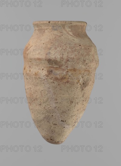 Vessel with hieratic inscription. Egyptian pottery, conical clay vessel tapering toward the bottom, irregular, widest at approx. 3/4 of the height. Narrow, slightly sloping shoulders; short, wide neck; very gently rounded, slightly flaring rim; pointed bottom. Handcrafted; upper part shoulders, neck, rim turned. Smooth surface, externally probably covered with a layer of engobe. Made of Nile clay NB2 Vienna System. In the lower part of the belly are remains of a hieratic inscription in black nbs. The vessel is complete, well preserved. Old Kingdom, ca. 2686–ca. 2181 BC, from Edfu. Dimensions: height 12.9 cm; rim diameter 5.5 cm; body diameter 7.8 cm. Comparative parallels cited Petrie, Dendera; Hope, Akhmim; Reisner; Brunton; Mace; Petrie, Abydos; Keiser et al.., An upright, rounded clay vessel with a narrow neck and flared rim sits against a plain gray background; the surface of the vessel shows a rough, weathered texture with patches of muted beige, tan, brown, and hints of reddish t...