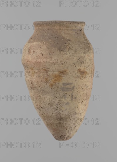 Vessel with hieratic inscription. Conical clay vessel tapering toward the bottom, irregular, widest at approx. 3/4 of the height. Narrow, slightly sloping shoulders; short, wide neck; very gently rounded, slightly flaring rim; pointed bottom. Handcrafted; upper part shoulders, neck, rim turned. Smooth surface, externally probably covered with a layer of engobe. Made of Nile clay NB2 Vienna System. Remains of a hieratic inscription in black in the lower part of the belly. Complete, well preserved. Old Kingdom, ca. 2686–2181 BC. Height 12.9 cm; rim diameter 5.5 cm; body diameter 7.8 cm. Comparative parallels noted in published Old Kingdom pottery studies., A weathered, bulbous ceramic vessel suspended against a plain light gray background, showing a rough, textured surface in shades of beige, tan, light brown, and hints of pink and ochre, with darker brown speckles and small pits; the rim is slightly thickened and rounded, the body tapers to a narrow, pointed base, and there are subtle v...