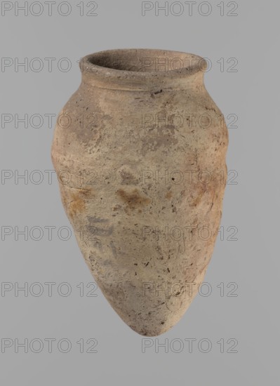 Vessel with hieratic inscription. Egyptian pottery. Conical clay vessel tapering toward the bottom, irregular, widest at approx. 3/4 of the height. Narrow, slightly sloping shoulders; short, wide neck; very gently rounded, slightly flaring rim; pointed bottom. Handcrafted; upper part shoulders, neck, rim thrown on a wheel. Smooth surface, exterior probably covered with an engobe. Made of Nile clay NB2 Vienna System. Remains of a hieratic inscription in black on the lower part of the belly. Complete and well preserved. Comparative parallels cited; previously dated to the Old Kingdom, ca. 2686–2181 BC, from Edfu. Dimensions: height 12.9 cm; rim diameter 5.5 cm; body diameter 7.8 cm., A single elongated clay vessel with a rounded rim and tapering pointed base is shown against a plain neutral background; the surface of the vessel is rough and mottled with a mix of earthy tones including beige, tan, light brown, gray, and hints of reddish-brown, with a few darker speckles and patches of sli...