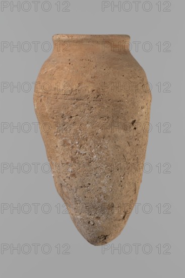Vessel with hieratic inscription. Conical clay vessel tapering toward the bottom, irregular; widest approx. 3/4 of the height. Narrow, only slightly sloping shoulders; short, wide neck; very gently rounded, slightly flaring rim; pointed bottom. Handcrafted; upper part shoulders, neck, rim turned. Smooth surface, exterior probably covered with a layer of engobe. In the widest part three shallow horizontal lines over a space of approx. 0.8 cm. Made of Nile clay NB2 Vienna System. Remains of a hieratic inscription in black sht on the lower body. Vessel complete, well-preserved. Old Kingdom, ca. 2686–2181 BC; findspot Edfu. Dimensions: height 14.4 cm; rim diameter 5.4 cm; body diameter 8.4 cm. Comparative parallels in Petrie, Reisner, Brunton, Mace, Keiser, and others., A single large, weathered clay vessel with a rounded shoulder and a tapered, pointed base suspended against a plain gray background; the surface shows rough, uneven texture with small pits and encrustations, and the vessel ...