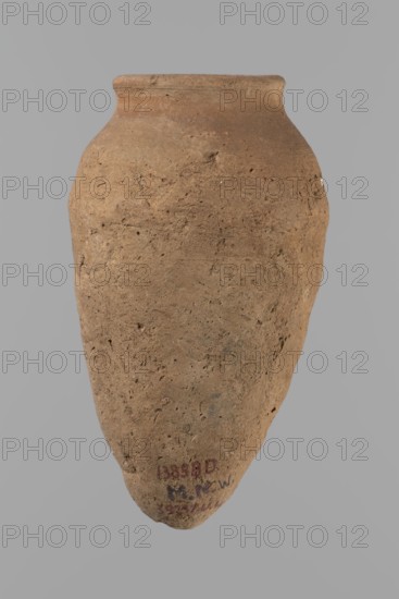 Vessel with hieratic inscription. Conical clay vessel tapering toward the bottom; irregular, widest at approx. 3/4 of the height. Narrow, only slightly sloping shoulders; short, wide neck; very gently rounded, slightly flaring rim; pointed bottom. Handcrafted — upper part shoulders, neck, rim turned. Smooth surface, externally probably covered with an engobe. In the widest part three shallow horizontal lines over approx. 0.8 cm. Made of Nile clay NB2 Vienna System. Remains of a hieratic inscription in black sht on the lower body. Vessel complete, well-preserved. Comparative parallels cited; earlier dated to the 4th–5th Dynasty / Old Kingdom, ca. 2686–2181 BC. Find spot: Edfu. Dimensions: height 14.4 cm; rim diameter 5.4 cm; body diameter 8.4 cm., A single elongated earthenware vessel with a rounded shoulder and a narrow, slightly flaring rim, showing a rough, textured surface with small pits and irregularities; the vessel is predominantly brown with variations of lighter and darker bro...