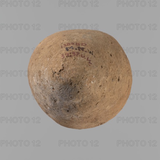 Vessel with hieratic inscription. Conical clay vessel tapering toward the bottom; irregular, widest at approx. 3/4 of the height. Narrow, only slightly sloping shoulders; short, wide neck; very gently rounded, slightly flaring rim; pointed bottom. Handcrafted, upper part shoulders, neck, rim turned. Smooth surface, externally probably covered with a layer of engobe. In the widest part three shallow horizontal lines over a space of approx. 0.8 cm. Made of Nile clay NB2 Vienna System. Remains of a hieratic inscription in black sht on the lower body. Vessel complete, well-preserved. Comparative parallels cited; earlier dated to the Old Kingdom ca. 2686–ca. 2181 BC, likely 4th–5th Dynasty. Dimensions: height 14.4 cm; rim diameter 5.4 cm; body diameter 8.4 cm., A roughly spherical object with a rough, pitted surface in shades of tan and light brown, showing a few darker brown and grayish patches and some small indentations and irregularities; the background is a uniform light gray.