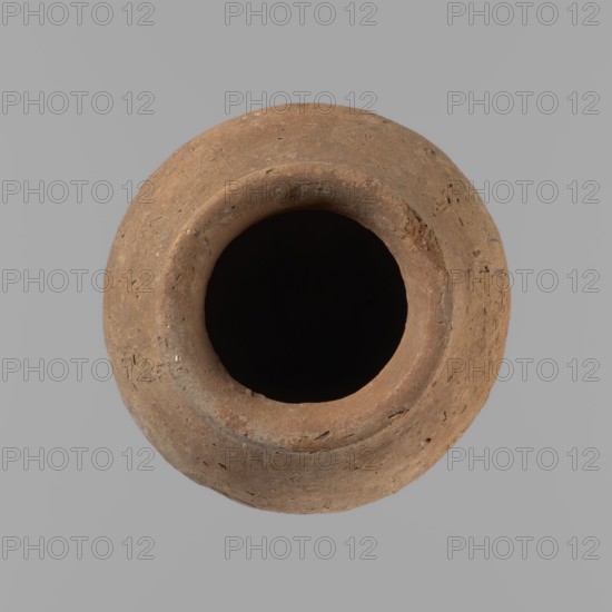 Vessel with hieratic inscription. Egyptian conical clay vessel, tapering toward the bottom, irregular, widest at approx. 3/4 of the height. Narrow, only slightly sloping shoulders; short, wide neck; very gently rounded, slightly flaring rim; pointed bottom. Handcrafted: upper part shoulders, neck, rim turned. Smooth surface, externally probably covered with a layer of engobe. Made of Nile clay NB2 Vienna System. Remains of a hieratic inscription in black in the lower part of the belly. Complete, well preserved. Old Kingdom, ca. 2686–2181 BC. Dimensions: height 12.5 cm; rim dia. 5.4 cm; belly dia. 8 cm. Comparative parallels cited Petrie, Hope, Reisner, Brunton, Mace, Keiser et al.., A round, worn clay vessel viewed from above with a wide dark opening at its center; the vessel surface shows a rough, textured appearance with small pits and specks and a warm brown to reddish-brown color against a solid light gray background.