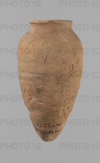 Vessel with hieratic inscription, Egyptian pottery, clay vessel, hand-made and turned in the upper part neck, spout. Conical shape tapering toward the bottom, irregular, widest at approx. 3/4 of the height; narrow, slightly sloping shoulders; short, wide neck; rounded, slightly flaring spout; pointed bottom. Smooth surface, light red color. Made of Nile clay NB2 Vienna System. Remains of a hieratic inscription in black on the lower part of the belly. Quite well preserved — rim slightly damaged. Comparative parallels cited; earlier dated to the 4th–5th Dynasty; Old Kingdom, Edfu. Dimensions: height 15.7 cm; rim diameter 5.7 cm; belly diameter 8.5 cm., A single weathered clay vessel with a rounded body tapering to a pointed base, shown against a plain light gray background; the vessel's surface is rough and pitted with visible tool marks and small indentations, and its rim is slightly flared and uneven. The overall color is a warm earthy brown with patches of darker brown and muted gray,...