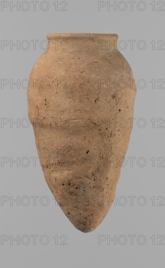 Vessel with hieratic inscription. Egyptian pottery, clay vessels, ceramics. Hand-made vessel, turned in the upper part neck, spout. Conical shape, tapering towards the bottom, irregular, widest approx. 3/4 of the height. Narrow, slightly sloping shoulders. Short, wide neck. Rounded, slightly flaring spout. Pointed bottom. Smooth surface. Color light red. Made of Nile clay NB2 Vienna System. In the lower part of the belly there are remains of a hieratic inscription in black. Quite well preserved; rim slightly damaged. Comparative material cited; earlier dated to the 4th–5th Dynasty Old Kingdom, ca. 2686–2181 BC. Find site: Edfu. Vessel dimensions: height 15.7 cm; rim diameter 5.7 cm; belly diameter 8.5 cm., A single large clay vessel is shown against a plain gray background; the vessel has a rounded shoulder that tapers to a pointed base and a short, slightly flared rim. The surface of the vessel is rough and textured with pits, small inclusions, and irregular marks. The dominant color ...