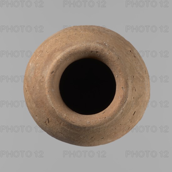 Vessel with hieratic inscription. Hand-made clay vessel, turned in the upper part neck, spout. Conical shape tapering toward a pointed bottom; irregular, widest at approx. 3/4 of the height. Narrow, slightly sloping shoulders; short, wide neck; rounded, slightly flaring spout. Smooth surface, light red color. Made of Nile clay NB2 Vienna System. Remains of a hieratic inscription in black on the lower part of the belly. Fairly well preserved; rim slightly damaged. Old Kingdom, Edfu. Height 15.7 cm; rim diameter 5.7 cm; belly diameter 8.5 cm. Comparative parallels: Petrie, Dendera; Hope, Akhmim; Reisner; Brunton; Mace; Petrie, Abydos; Keiser et al.; dated ca. 2686–2181 BC., A round, terracotta-colored clay vessel with a wide, dark interior opening sits against a smooth gray background, showing a rough, textured surface with small pits and flecks and subtle variations of brown and tan tones.