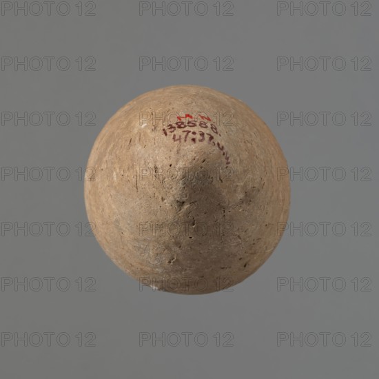 Vessel with hieratic inscription, Egyptian ceramic conical vessel tapering toward the bottom, handcrafted with the upper part shoulders, neck, rim turned. Narrow, sloping shoulders; short, wide neck; very gently rounded, flaring rim; pointed bottom. Smooth surface, externally probably covered with engobe. Made of Nile clay NB2 Vienna System. At the widest diameter three shallow horizontal incised lines two 0.2 cm apart, the third 0.5 cm from the second, made before firing. Remains of a hieratic inscription in black on the lower body. Rim slightly damaged. Old Kingdom, Edfu; height 16 cm, diameter 6.3 cm rim, diameter 9.4 cm body., A round, roughly spherical object with a textured, earthy surface in shades of tan and light brown floats against a smooth grey background; the object shows small pits and irregularities on its surface and a few darker brown spots, with a curved area near the top that has traces of red pigment.